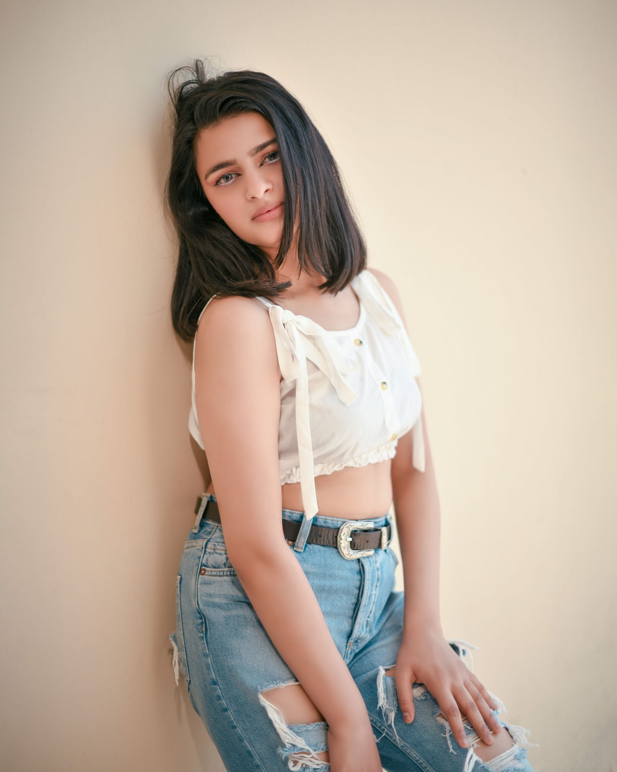 Chic young woman leaning against a beige wall in a trendy denim outfit, showcasing a modern fashion style.